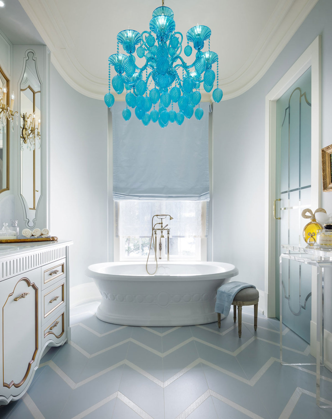 Un candelabro de cristal azul destacado sobre una bañera flotante, pisos con motivos de chevron y gab